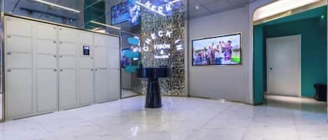 A lobby with a marble floor, lockers, a reception desk, and a wall-mounted TV screen.