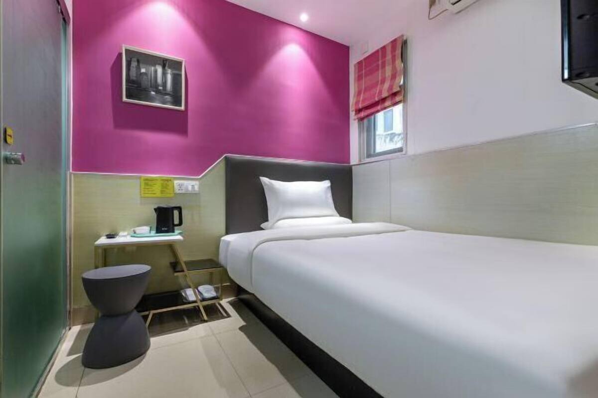 A hotel room with a bed, a small table with a kettle, a chair, and a picture on the wall.