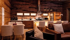 A cozy, rustic interior with a wooden wall, a central island with a sink, a dining area with chairs, and a leather sofa. - Cozy Mountain Getaway with Hot Tub  Sleeps Your Whole Group (Revelstoke)