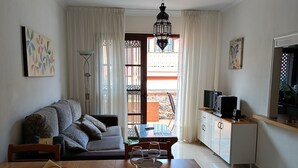 A living room with a sofa, dining table, chairs, a TV, and a balcony with a view. - Yellow mountain in paradise (Costa del Silencio)