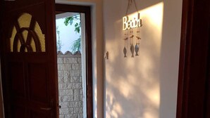 A hallway with a wooden door, a wall-mounted light fixture spelling "Beau," and a stone wall outside.