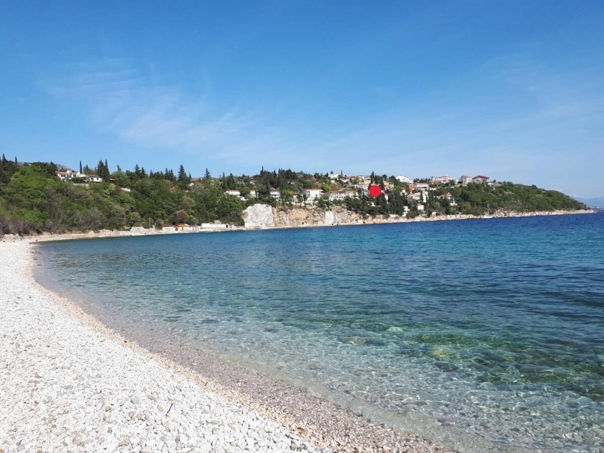 Una platja costanera amb aigua cristal·lina, sorra petita i edificis al fons d'una collada.