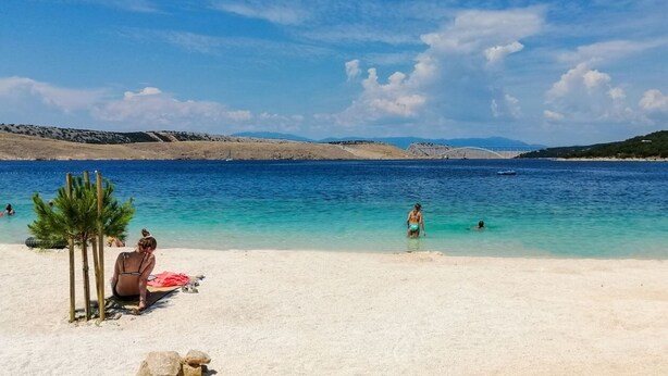 A beach with clear blue water, a sandy shore, and a few people swimming.
