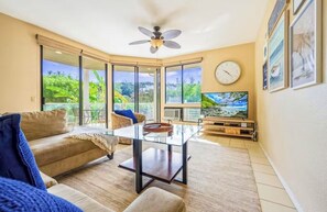 A living room with a glass coffee table, a sofa, a television, and a ceiling fan. - Spacious 3BR/2BA Condo in Wailea – Walk to Beach & Shops! (Wailea-Makena)