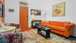 A living room with a vibrant orange sofa, a colorful patterned rug, and a coffee table. - The Tangerine - Walk to Restaurants, Shops, Bars! (Hot Springs)