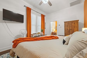 Quarto com cama, televisão de tela plana, ventoinha no teto e guarda-roupa de madeira.