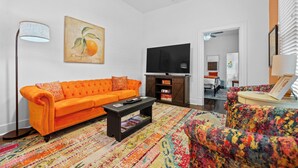 A living room with an orange sofa, a black entertainment unit, and a colorful rug. - The Tangerine - Walk to Restaurants, Shops, Bars! (Hot Springs)
