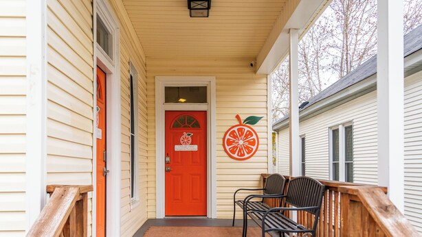 A porch with a red door, two black chairs, and a wooden railing. - The Tangerine - Walk to Restaurants, Shops, Bars! (Hot Springs)