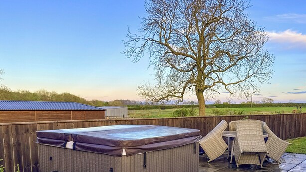 A hot tub with steps, a covered seating area, and a view of a tree and open fields.