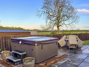 Een hottub met treden, een overdekt zitgedeelte en uitzicht op een boom en open velden.