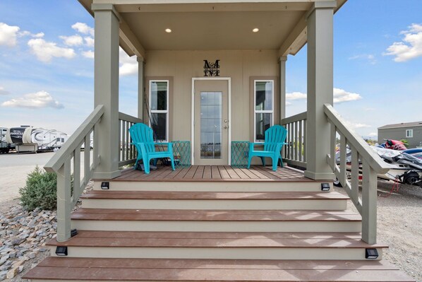 A covered porch with two chairs, a door, and a railing.