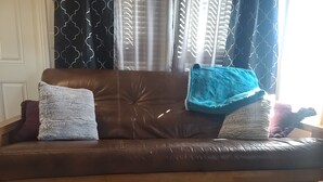 Un sofá de cuero marrón con dos almohadas mullidas y una manta azul.