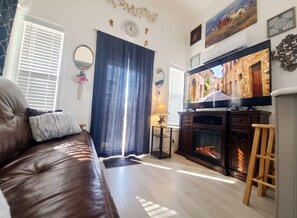A living room with a leather sofa, a fireplace, a television, and a large window with curtains. - Tiny River Home Beach, Pool, Spa, Boat Launch, Gym, Fishing Pond, Playground (Ehrenberg)
