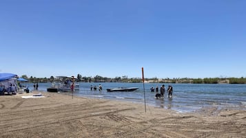 Une plage avec un bateau amarré, des personnes près de l’eau et un ciel dégagé.