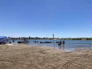 A beach with a boat docked, people near the water, and a clear sky.