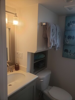 Un baño con un lavamanos blanco, un inodoro y una repisa con toallas.