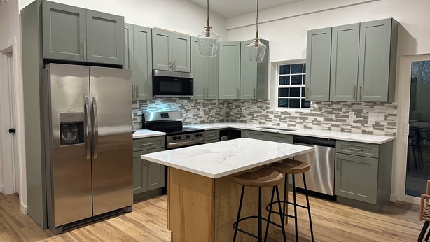 Una cocina moderna con armarios grises, electrodomésticos de acero inoxidable, encimera de mármol y taburetes de madera.