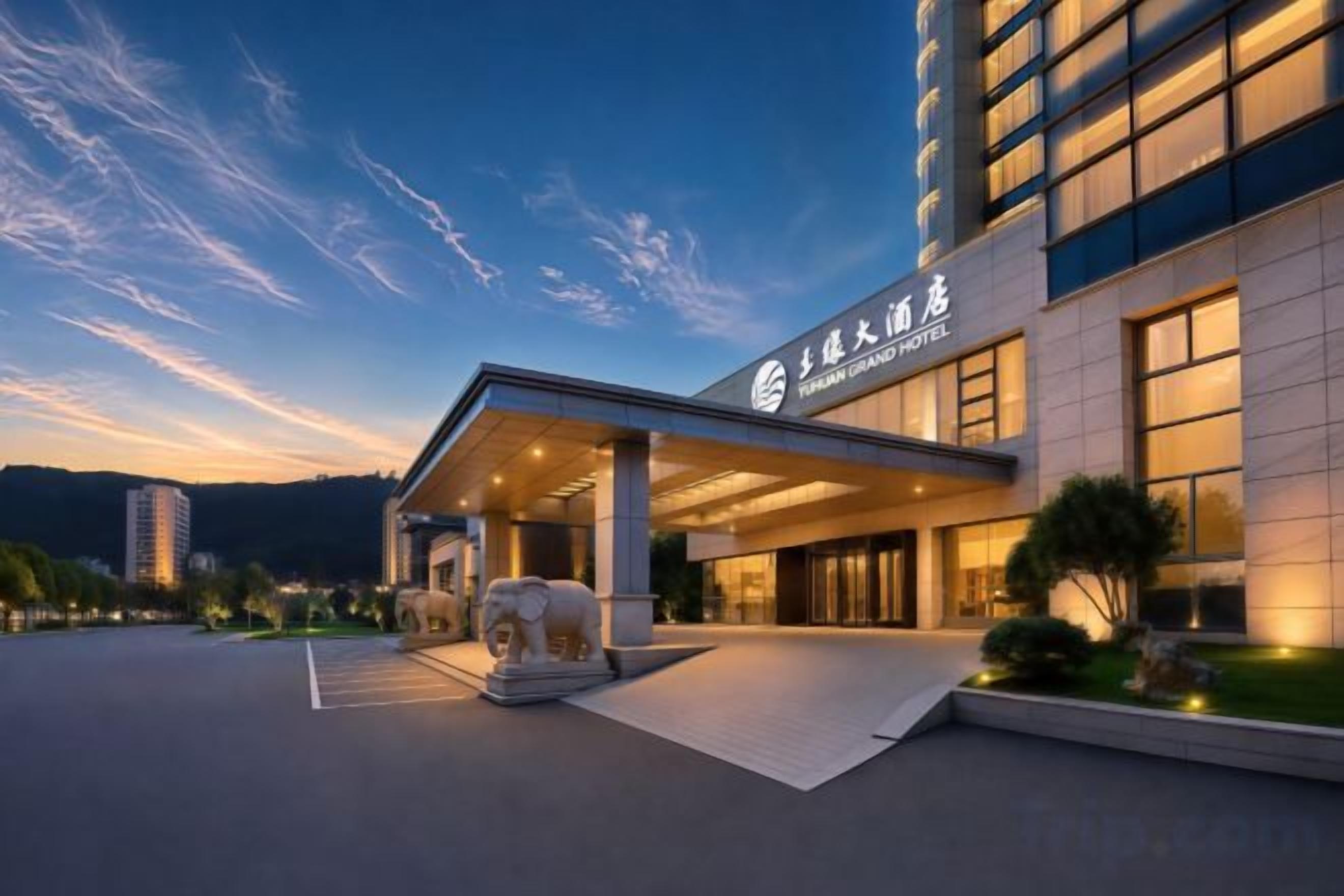 A hotel entrance with a covered walkway, a large elephant sculpture, and a mountainous backdrop.