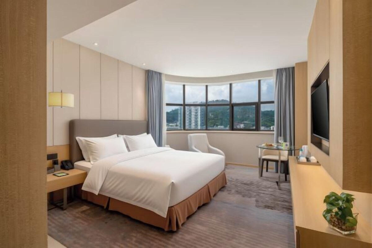 Une chambre d’hôtel avec un grand lit, un bureau, une chaise, une télévision et une fenêtre donnant sur la ville.