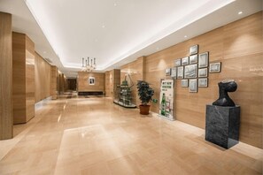 A hotel corridor with a polished floor, wooden walls, a chandelier, framed pictures, a potted plant, and a sculpture. - Yuhuan Grand Hotel (Yuhuan)