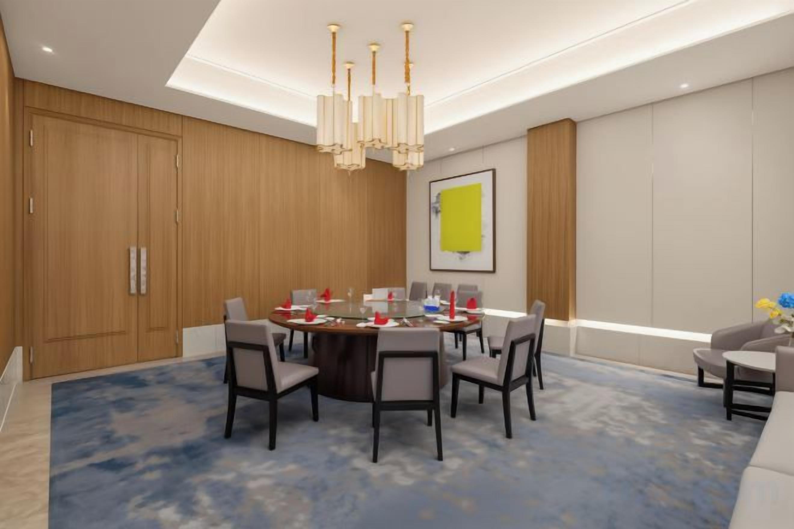 A conference room with a round table, chairs, a chandelier, and a blue carpet.