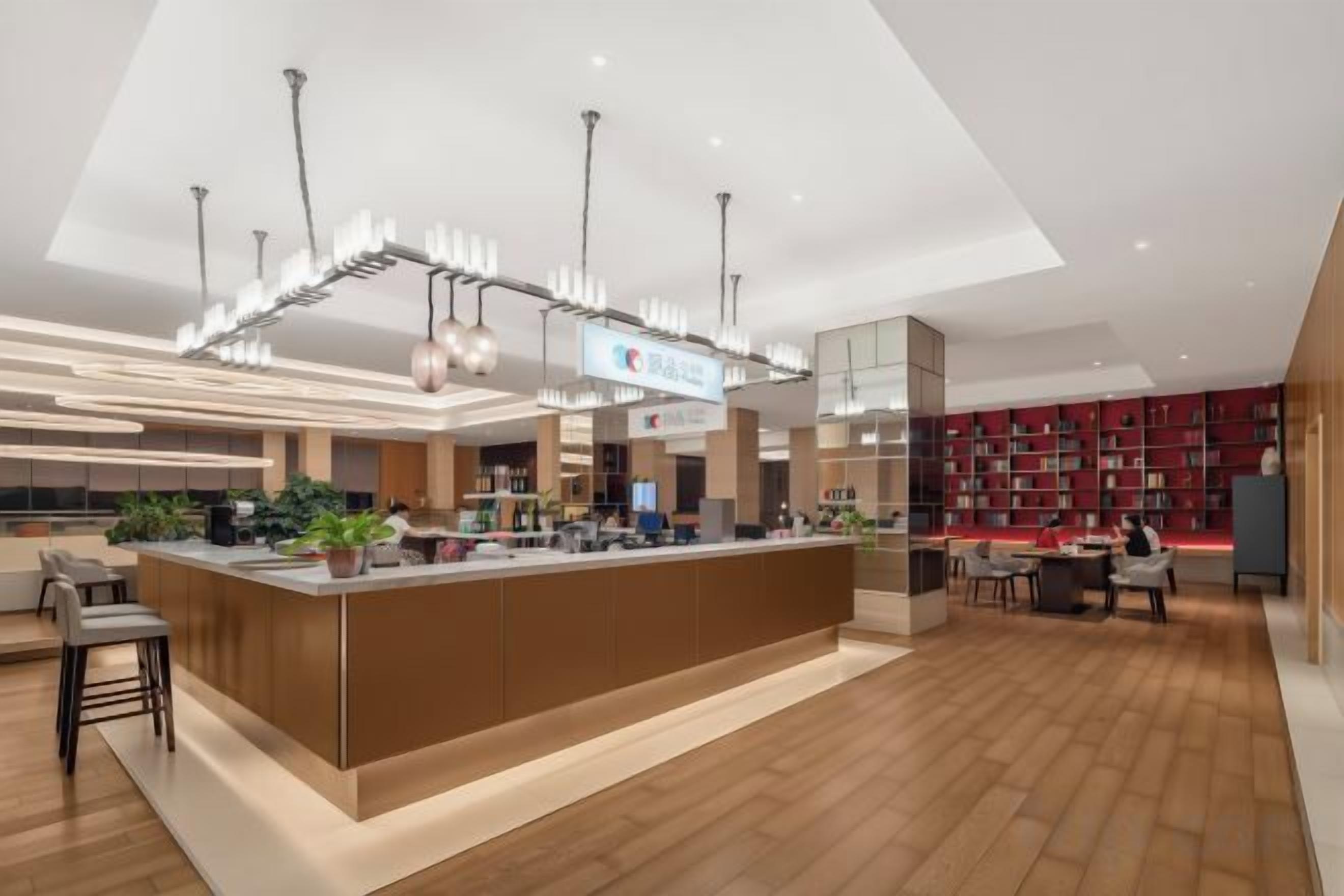 A modern hotel lobby with a central reception desk, seating area, and a large bookshelf.
