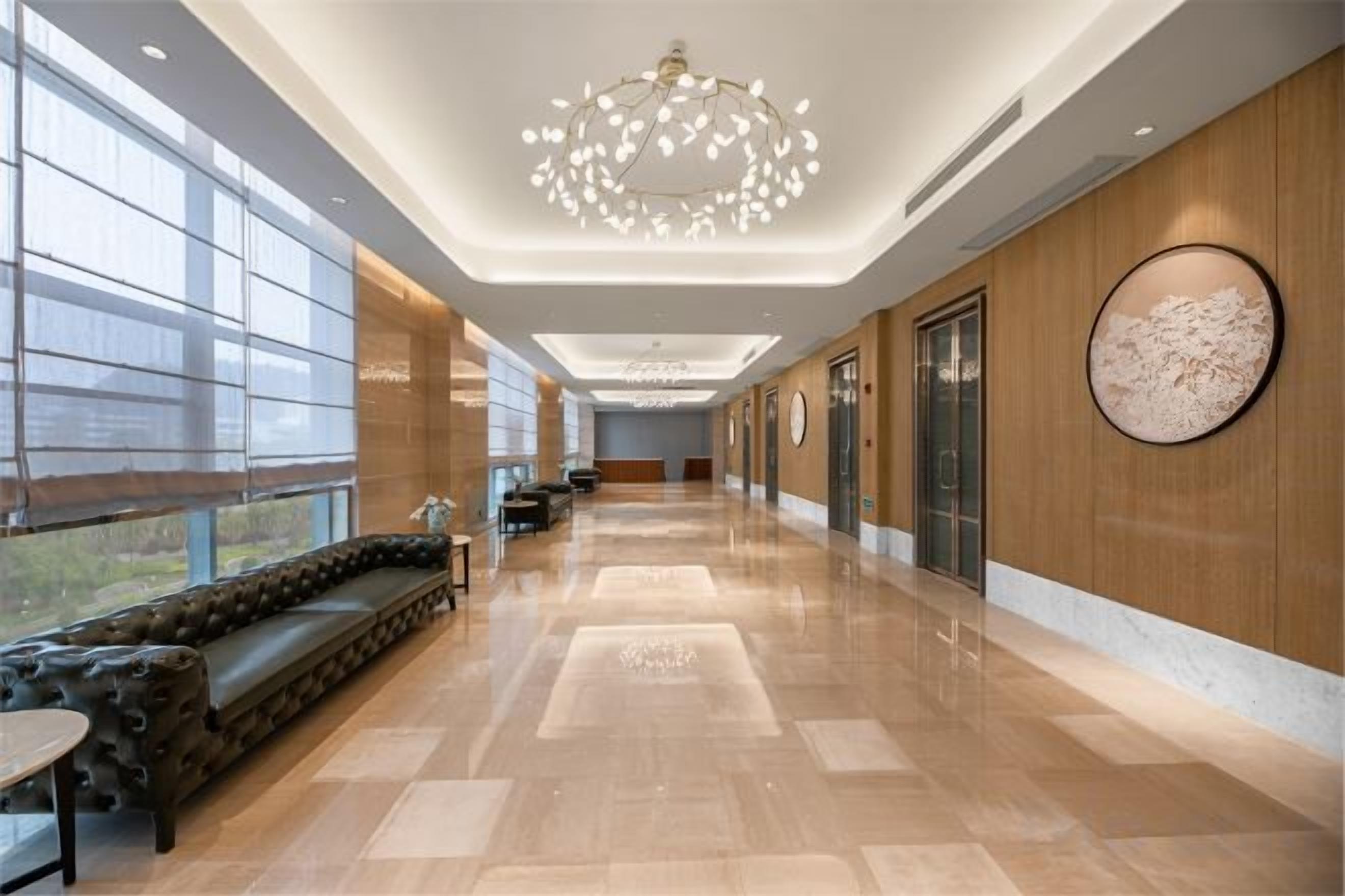 A hotel lobby with a long reception desk, a seating area, and a large chandelier.