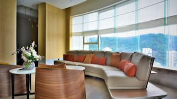 A modern living room with a curved sofa, a round table, and a large window offering a city view.