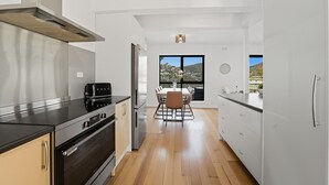 Una cocina moderna con electrodomésticos de acero inoxidable, un comedor con mesa y sillas, y grandes ventanales que ofrecen vistas al exterior.