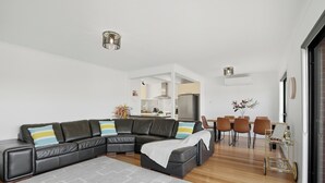 Una sala de estar moderna con un sofá seccional, un comedor con sillas y una cocina al fondo.