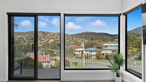 Habitación con ventanas amplias que ofrecen vistas a una zona residencial y colinas.