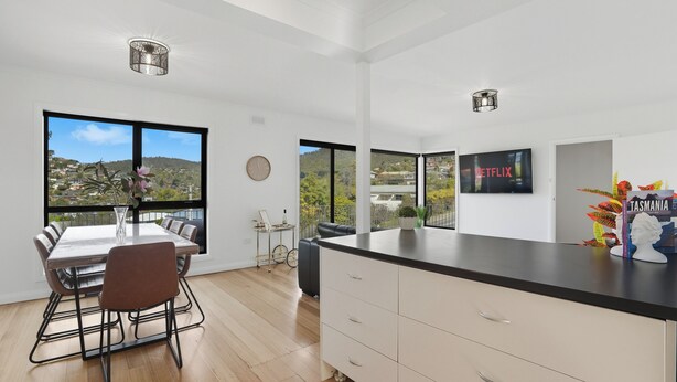 Una cocina moderna con una isla grande, comedor y ventanas amplias que ofrecen vistas a las colinas.