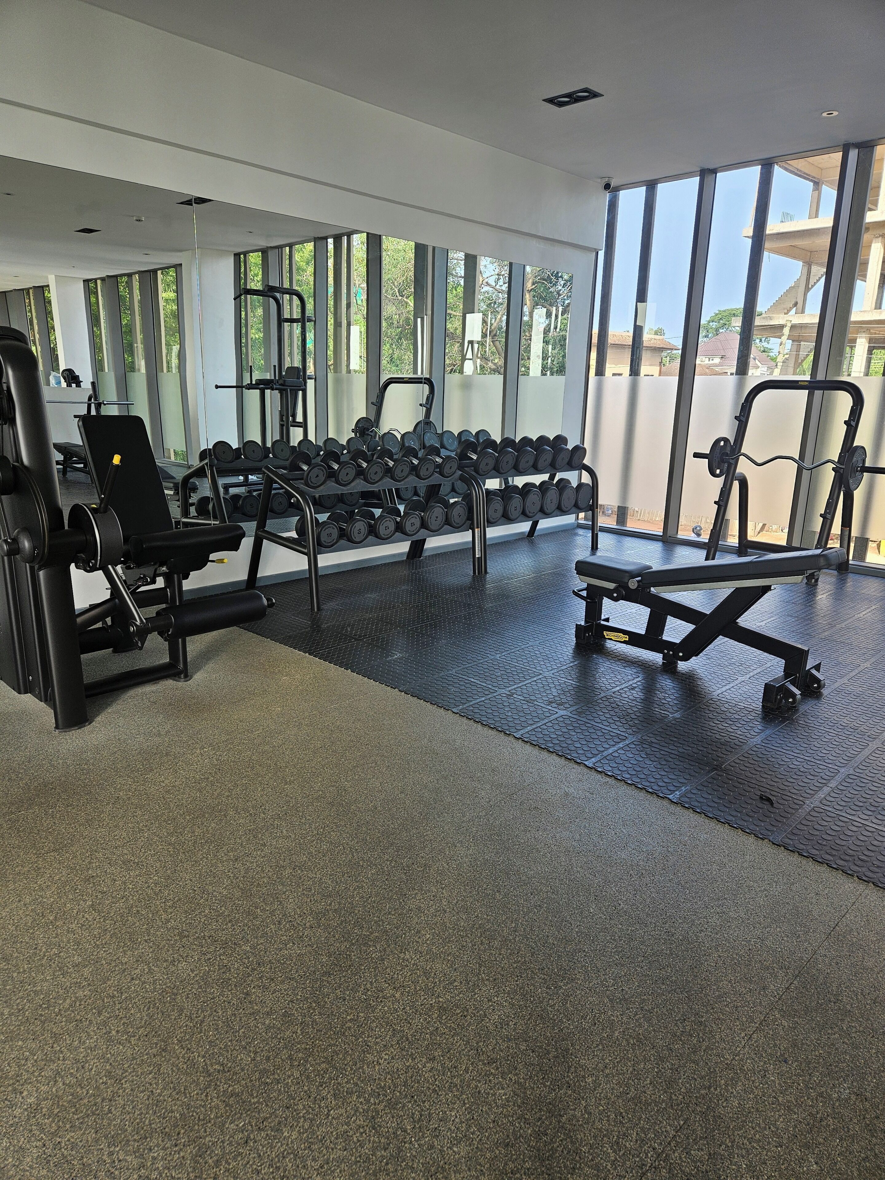 A gym with exercise equipment, weight racks, and large windows.