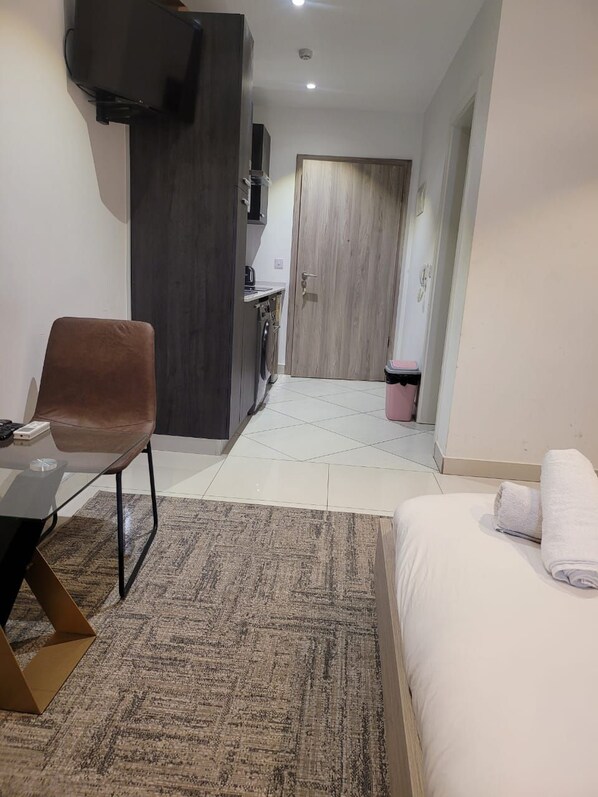 Habitación de hotel con cama, escritorio, silla, televisor, armario y una pequeña kitchenette.