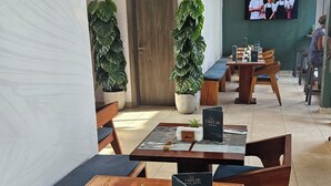 A restaurant with wooden tables and benches, potted plants, and a TV screen on the wall. - RT properties at the Lennox  (Accra)