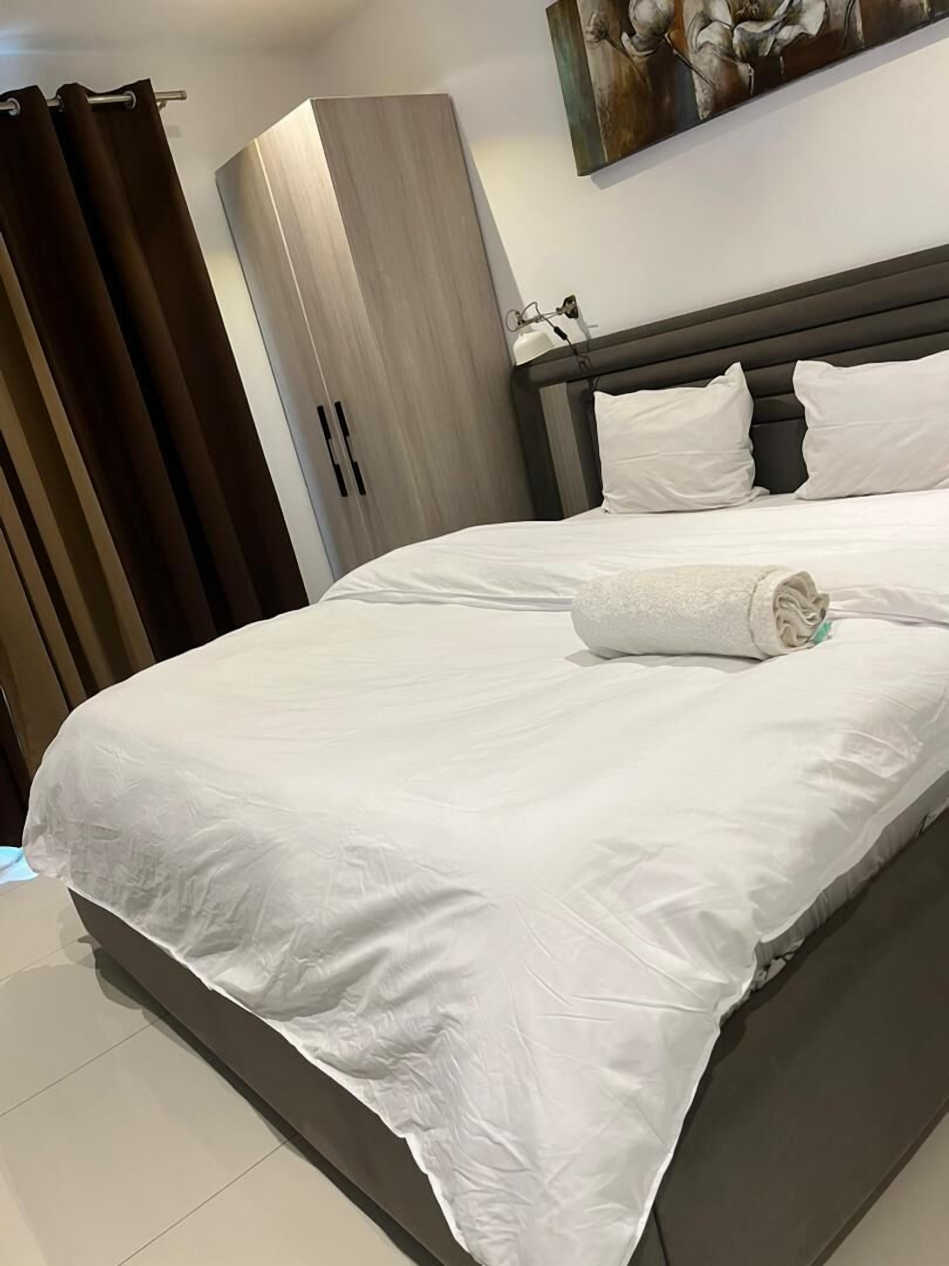 A neatly made bed with white linens, a dark headboard, and a white pillow.