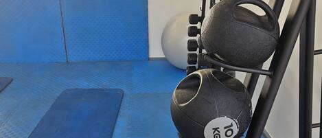 A gym with a rack of kettlebells, blue mats, and a large exercise ball.