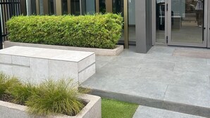 A modern building exterior with vertical glass panels, a landscaped area with grass and shrubs, and a paved entrance. - RT properties at the Lennox  (Accra)