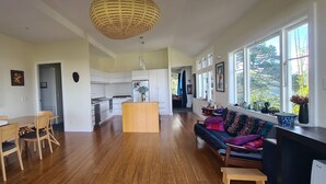 Amplia sala de estar con una mesa y sillas de madera, un sofá con cojines coloridos, y una cocina al fondo.