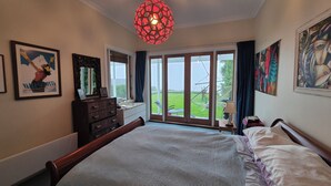 Un dormitorio con una cama grande, un aparador, un espejo y una ventana con vistas a un jardín.