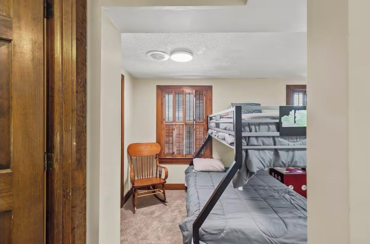 A small, cozy bedroom with a bunk bed, a wooden chair, and a window with shutters.
