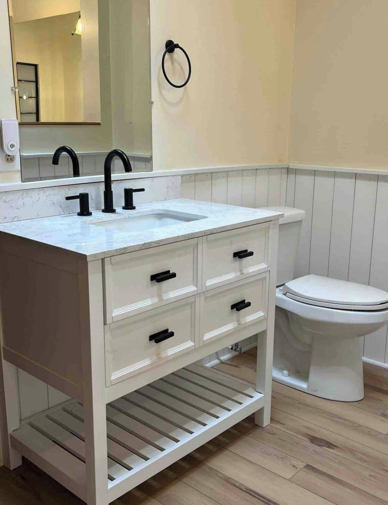 A bathroom with a white vanity, black faucets, a mirror, and a toilet.