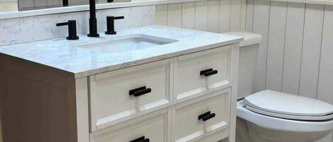 A bathroom with a white vanity, black faucets, a mirror, and a toilet.