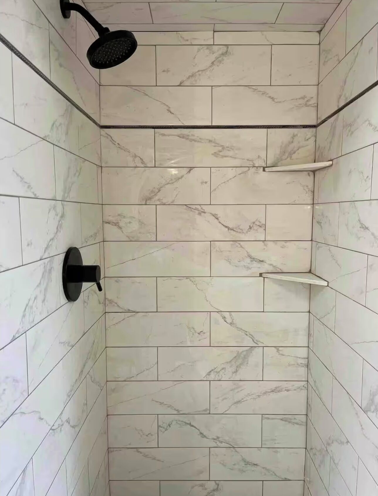 A shower with a handheld showerhead and a wall-mounted control.