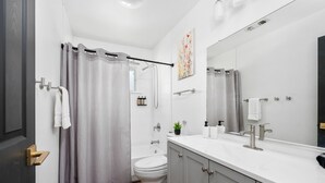 Un baño moderno con cortina de ducha, inodoro, lavabo y espejo.