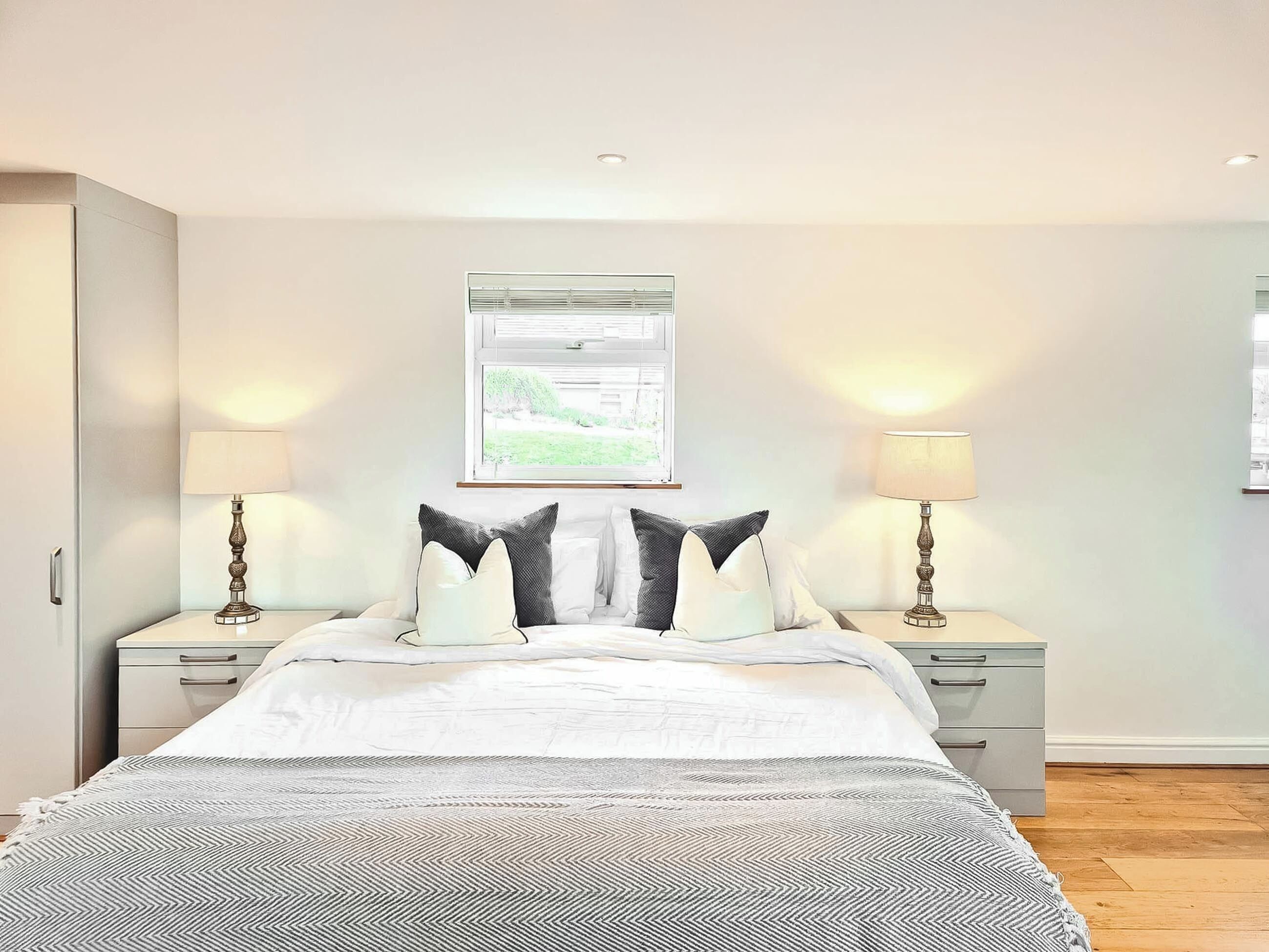 A bedroom with a bed, two bedside tables, a nightstand, a window with a view, and a ceiling light.