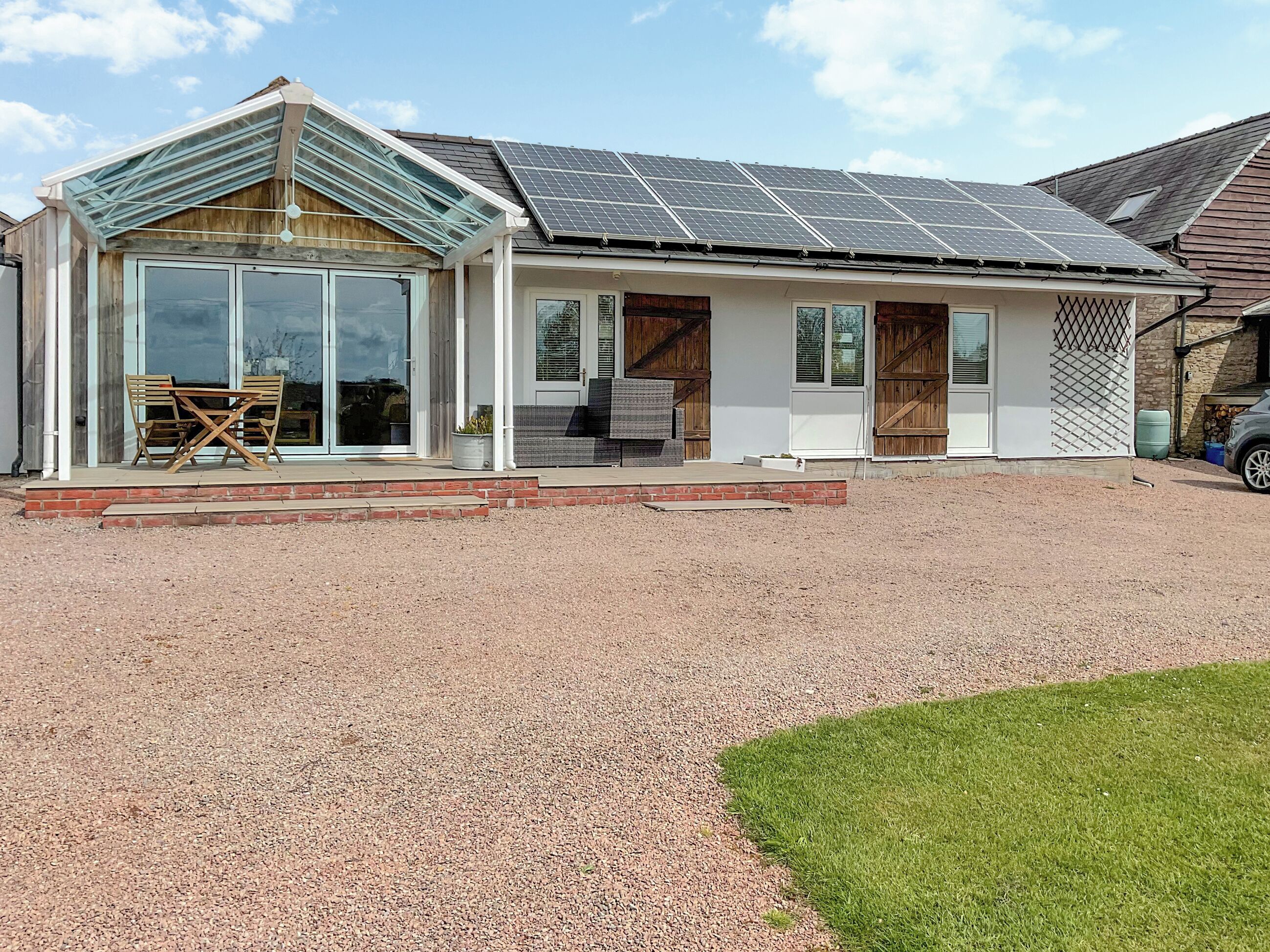 Ein modernes Haus mit Solaranlage auf dem Dach, einem Glastür-Eingang und einer Terrasse mit Gartenmöbeln.