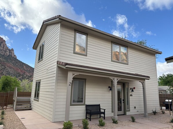 A two-story house with a porch, a bench, and a mountain view.
