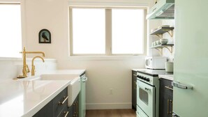 A kitchen with a white countertop, a gold faucet, a vintage stove, and a window above the sink.
