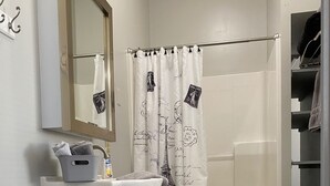 A bathroom with a white sink, a toilet, a shower curtain with Eiffel Tower prints, a wooden basket, and a grey rug. - Hip Suite-1st Floor - Arts District/Farmers Mkt/Cafes/Breweries-Near Lake George (Glens Falls)